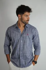 Camisa de manga larga con estampado de rayas verticales finas en tonos azules. Presenta cuello clásico, cierre frontal con botones y un pequeño logo bordado en color contrastante en el pecho.