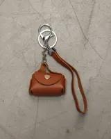 Llavero con forma de mini cartera color marrón, con cierre de broche dorado y tira de cuero. Incluye gancho metálico plateado.