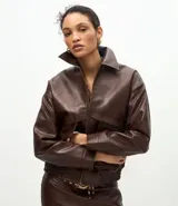 Campera de cuero sintético color marrón oscuro, con cuello clásico, cierre frontal metálico, dos bolsillos frontales amplios con solapa y ruedo con elástico.