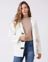 Campera tipo teddy de textura suave y esponjosa en color blanco, con cierre frontal mediante botones y detalles de apliques en cuero sintético negro en la solapa. Presenta bolsillos frontales y un diseño cómodo y abrigado.