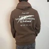 Canguro con capucha color marrón, con estampado gráfico en la espalda que incluye texto y elementos decorativos.