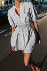 Vestido corto de color celeste con estampado floral, cuello redondo con volante y escote en pico. Presenta mangas cortas abullonadas con puños elásticos y cintura con nido de abeja elástico.