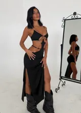 Vestido largo negro con aberturas laterales, escote halter con aros metálicos y espalda descubierta.