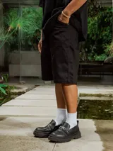 Bermuda negra de gabardina, corte ancho y largo, con bolsillos laterales.