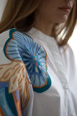 Vestido camisero corto color amarillo pálido con estampado floral en el hombro izquierdo y cinturón de tela con diseño geométrico.