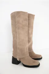 Bota de caña alta confeccionada en cuero gamuzado color marrón, con diseño de polaina desmontable. Presenta punta cuadrada, taco bloque negro y suela a tono.