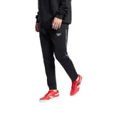 Pantalón de jogging negro con cintura elástica, corte ajustado y logo de Reebok estampado en blanco. Presenta una franja blanca vertical a lo largo de la pierna.
