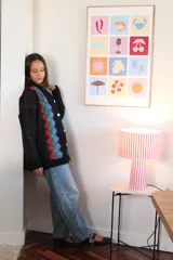 Cardigan de punto negro con diseño de rombos verticales en colores vibrantes como verde, rojo y violeta. Presenta cierre frontal con botones blancos, cuello redondo y mangas largas.