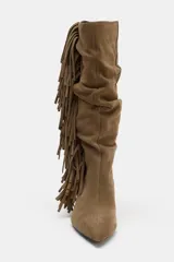 Bota de caña alta confeccionada en serraje, con diseño fruncido y detalle de flecos laterales. Presenta tacón kitten y acabado en punta.