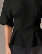 Remera negra de diseño estructurado con silueta entallada, mangas amplias y detalles de pinzas en la cintura que realzan la figura.