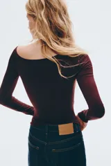 Remera de manga larga color bordó oscuro, con escote asimétrico de un solo hombro y frunces laterales que generan un efecto drapeado.