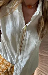 Collar estilo bolo tie con cordón de cuero marrón y pieza central metálica dorada, acompañado por una gargantilla de cordón fino con cuentas de resina color ámbar.