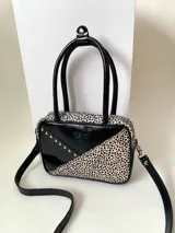Cartera rígida negra con detalles en rojo y tachas plateadas. Tiene herrajes y cierre metálico plateado marca YKK, asa fina para llevar al hombro o en la mano y correa larga extra regulable. El interior es forrado, tiene un bolsillo con cierre enmarcado en cuero, y un segundo bolsillo plaqué.