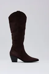 Bota de caña alta confeccionada en gamuza color chocolate, con diseño de estilo western, punta fina y taco cuadrado de altura media.