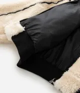 Campera de fleece color beige con diseño de paneles, costuras expuestas en color negro y cierre frontal. Posee cuello alto, mangas largas con puños elásticos y forro interior.