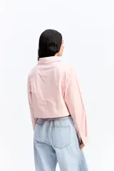 Camisa crop de corte relajado, con cuello clásico, cierre frontal de botones y mangas largas con puños. Confeccionada en algodón, presenta un diseño versátil y moderno.