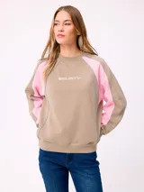 Buzo de cuello redondo Rusty, con diseño color block en tonos beige y rosado. Presenta mangas raglán con costuras decorativas y logo de la marca estampado en el centro del pecho.