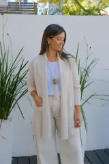 Saco abierto tipo cárdigan color crudo, de corte recto y largo medio, con mangas largas y dos bolsillos frontales aplicados.