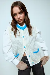 Chaleco tejido de punto con diseño de rayas horizontales en tonos gris y blanco. Presenta cuello redondo, cierre frontal con botones en color celeste y dos bolsillos delanteros con bordes en contraste de color celeste.