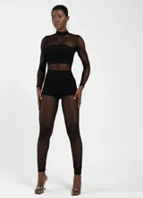 Jumpsuit de manga larga con cuello alto, confeccionado en tejido de red con paneles opacos en el torso y la zona de la cadera. Presenta un diseño ajustado al cuerpo con textura de malla.