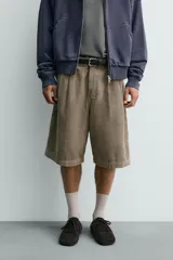 Bermuda wide fit color beige, confeccionada en pana de algodón. Presenta pliegues frontales en la cintura, bolsillos delanteros y bolsillos traseros de plastrón. Cierre frontal con cremallera y botón.