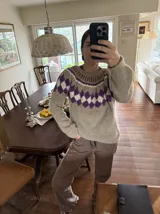 Sweater tejido a mano en mohair, de color marrón con diseño de canesú estampado con corazones fucsias y detalles geométricos en tonos beige y rosado. Presenta cuello redondo y mangas largas.