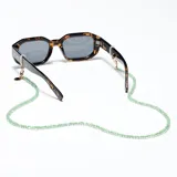 Correa para lentes Meller modelo Yaro, compuesta por cuentas de cristal semitransparentes en color verde. Incluye enganches metálicos dorados ajustables para gafas y una chapa de acero inoxidable con el logo de la marca grabado.