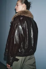 Chaqueta de efecto cuero con acabado brillante, cuello de solapa con aplicación de pelo sintético extraíble, cierre frontal cruzado con botones, mangas largas con puños ajustables y bajo elástico. Cuenta con forro interior acolchado.