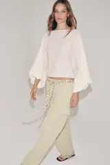 Cuerpo de punto color crudo, con cuello barco y mangas largas abullonadas con sisa ancha y puños ajustados.