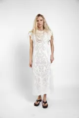 Vestido largo de crochet color crudo, con mangas cortas con volados y aberturas laterales, confeccionado en tejido calado de algodón con diseño ornamentado.