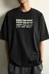 Camiseta de corte relajado color negro, con cuello redondo y manga corta. Presenta bordados a contraste en el frente con la frase 'Drop the beat' repetida en diferentes estilos tipográficos.