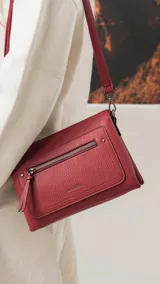 Bandolera de tamaño mediano en color gris, confeccionada en símil cuero con textura granulada. Presenta un bolsillo frontal con cierre, herrajes metálicos oscuros y correa ajustable y desmontable.