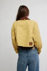 Campera corta de sarga de inspiración workwear, color amarillo con cuello en contraste marrón, bolsillos con solapa en el pecho y cierre frontal con botones.