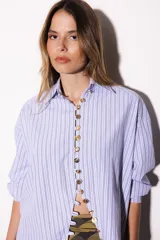 Camisa oversize a rayas celestes y blancas, con cuello camisero, manga larga y hilera de botones dorados metálicos.