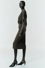 Vestido midi de tejido piqué en color marrón oscuro jaspeado, con escote en pico cruzado y mangas cortas. Presenta detalle de frunces en la cintura y un cinturón integrado con hebilla metálica a contraste.