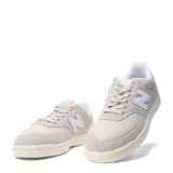Championes urbanos New Balance modelo Court, color gris claro con detalles en blanco. Confeccionados en una combinación de gamuza y malla, presentan el logo 'N' característico en los laterales y una suela de goma en tono crema.