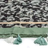 Pashmina estampada con diseño abstracto en tonos verde, negro y beige. Termina en una guarda lisa color verde y flecos blancos y verde agua.