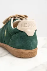 Zapatillas bajas color verde oscuro de gamuza con cordones color beige y suela de goma color marrón.