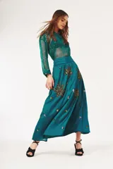 Falda larga color turquesa con cintura alta y apliques bordados de lentejuelas doradas y plateadas en forma de hojas o flores.