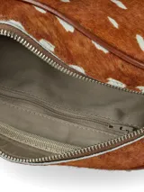 Bandolera compacta de cuero con pelo, con estampado animal print simil ciervo en tonos marrón y blanco. Cuenta con detalles de ribetes en cuero liso marrón, correa ajustable y un aplique frontal con el logo de la marca grabado.