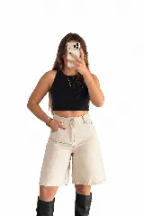 Bermuda de jean color beige, de tiro alto y corte ancho hasta las rodillas, con bolsillos laterales y traseros, y cierre frontal con botón y cremallera.