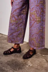 Pantalón jean de tiro alto y corte wide leg, con estampado de hojas grandes en tonos morados y fondo con patrón a cuadros.