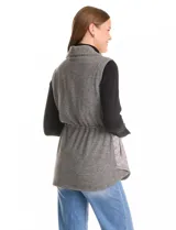 Chaleco gris de diseño híbrido, con frente capitoneado de patrón ondulado y espalda de tejido de punto. Presenta cuello con solapa, cierre frontal con botones a presión metálicos, cordón de ajuste en la cintura y bajo curvo.