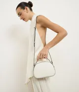 Bolso pequeño de Satinato con forma redondeada, color blanco y detalles en negro. Cuenta con asa corta de mano y correa larga ajustable para llevar cruzado.