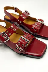 Sandalias rojas de cuero con punta cuadrada, dos tiras con hebillas plateadas y ojales.