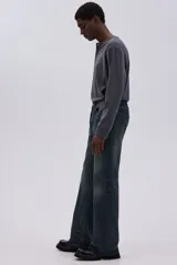 Jean de cinco bolsillos en denim de algodón rígido, color azul oscuro con efecto desgastado y lavado. Corte de tiro alto con pierna acampanada amplia.