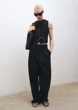 Chaleco de sastre color negro, con cuello en pico y cierre frontal de botones. Presenta un diseño recto, sin mangas y cuenta con dos bolsillos de ribete en la parte delantera.