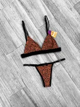 Conjunto de lencería compuesto por un corpiño triangular y una bombacha tipo tanga, ambos con estampado animal print en tonos naranja y negro, con detalles de elásticos negros y herrajes metálicos.