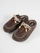 Mocasines tipo mule color marrón con textura de gamuza, costuras decorativas en el borde y cordones con cuentas de acrílico de colores.