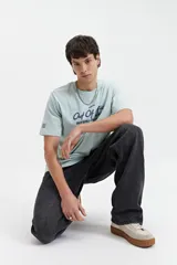 Remera celeste de manga corta con cuello redondo y estampado con la frase "Out of Office All Chasing Dream" en color negro.